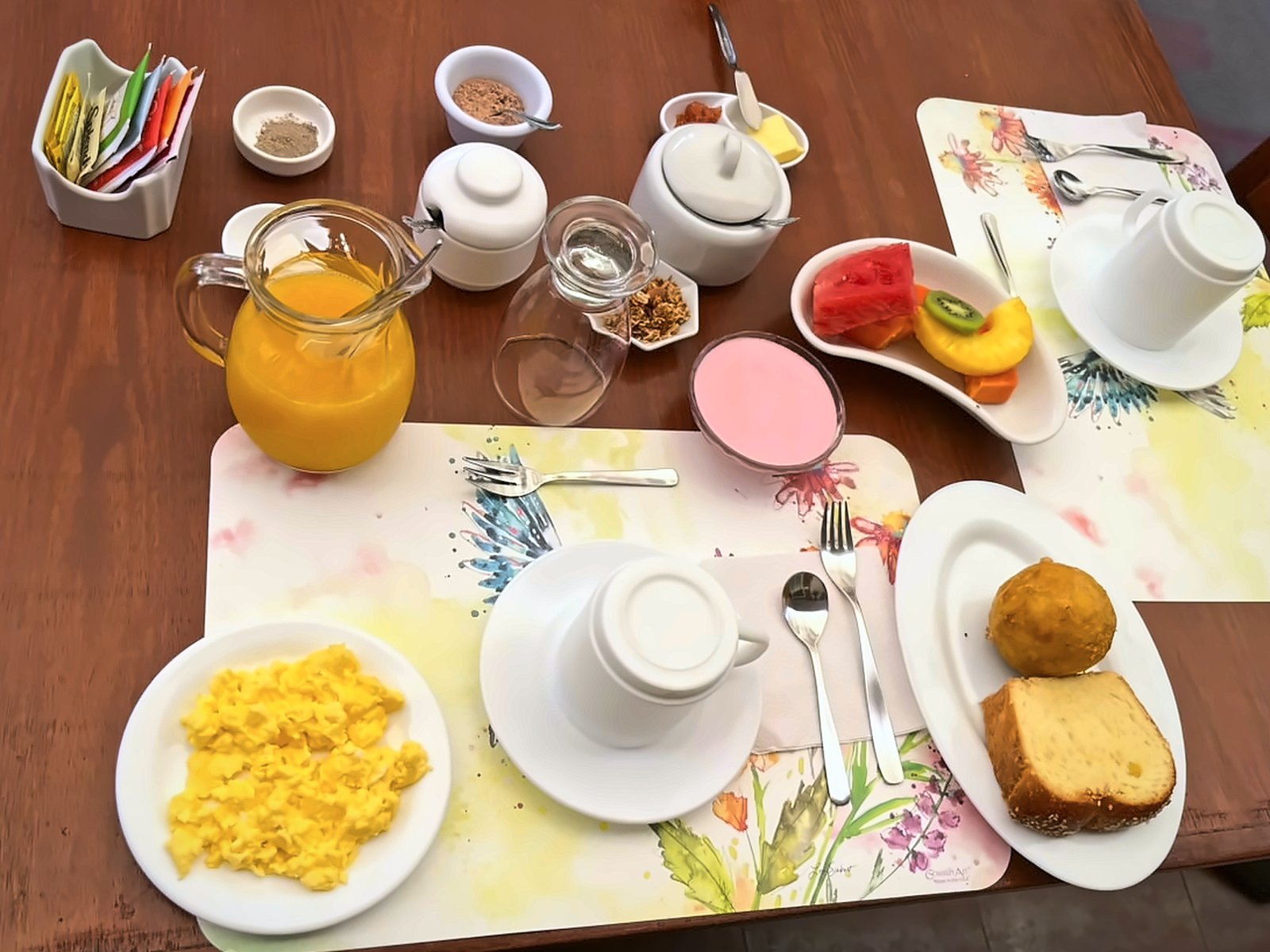 Mesa de desayuno en Mindo Real Lodge con huevos revueltos, frutas, yogurt, jugo, té o café y pan de la casa